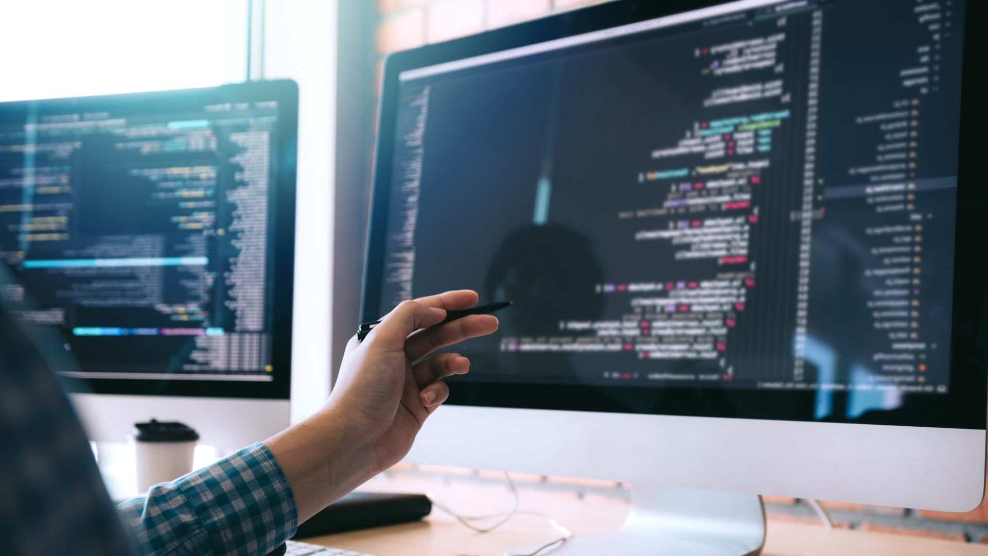 Developer working on website and web app code on computer screens